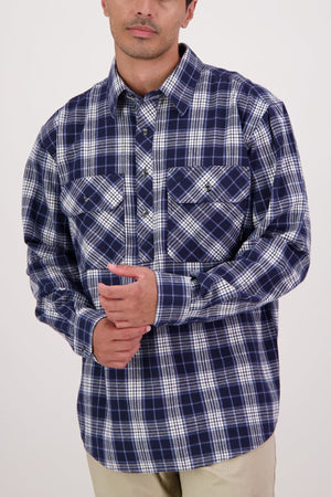 A person wears the Swanndri Barn Shirt—100% cotton, blue and white plaid—with beige pants against a plain light background, hands clasped in front. Ideal for easy winter layering.