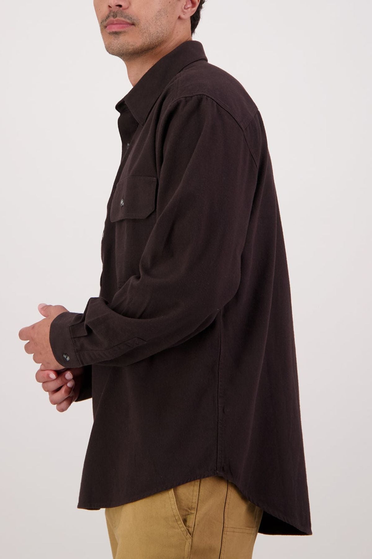 A person in a dark brown Swanndri Barn Shirt and light tan pants, facing left with bent arms, shown from mid-thigh up against a plain light background—combining classic heritage style for ideal winter layering.