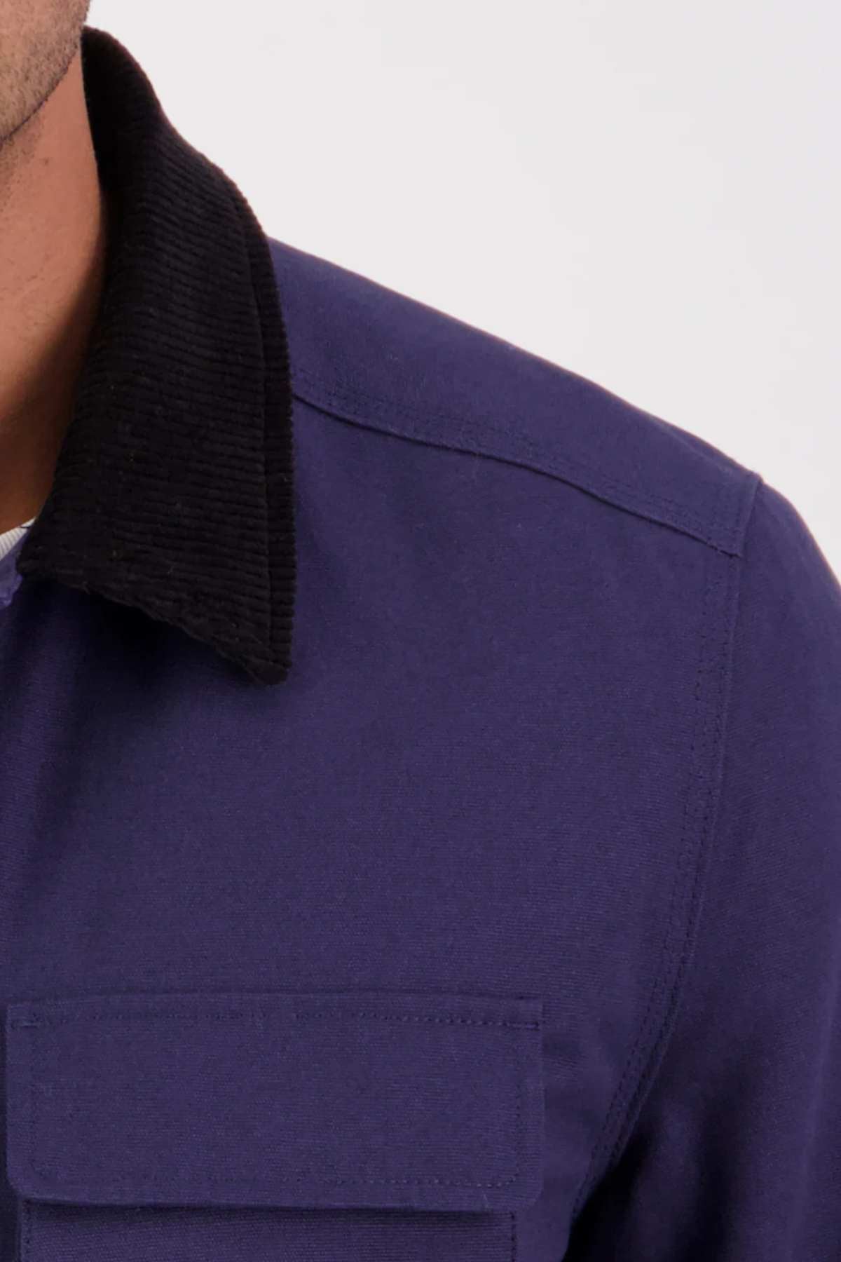 A close-up of a person wearing the Swanndri Barrytown v3 Canvas Work Jacket in dark blue, featuring a black corduroy collar and chest pocket, set against a plain light background.