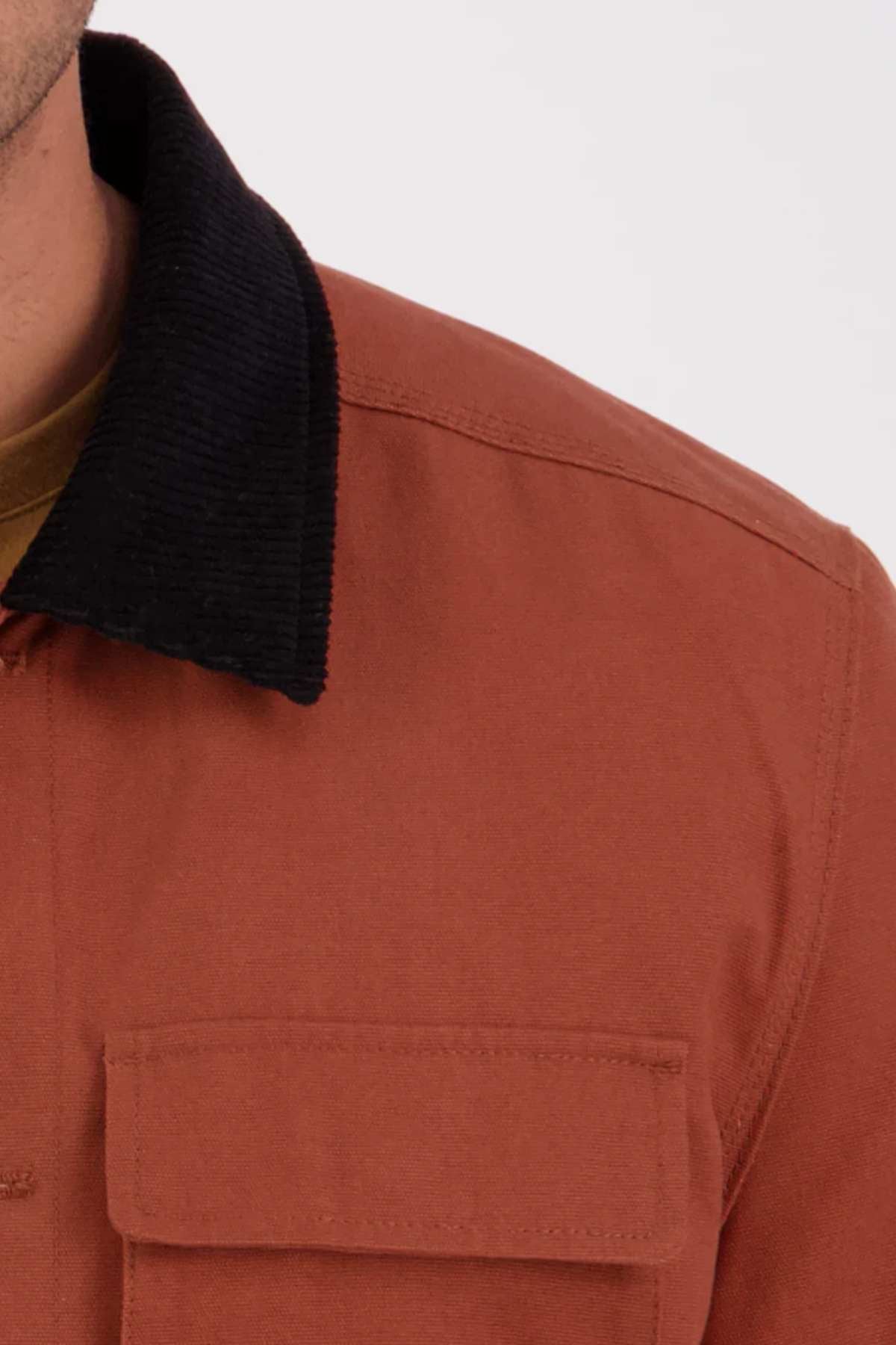 A close-up of the Swanndri Barrytown v3 Canvas Work Jacket, made from 100% cotton canvas with reinforced stitching, featuring a rust body, black corduroy collar, and front chest pocket with part of the shoulder and collar visible.
