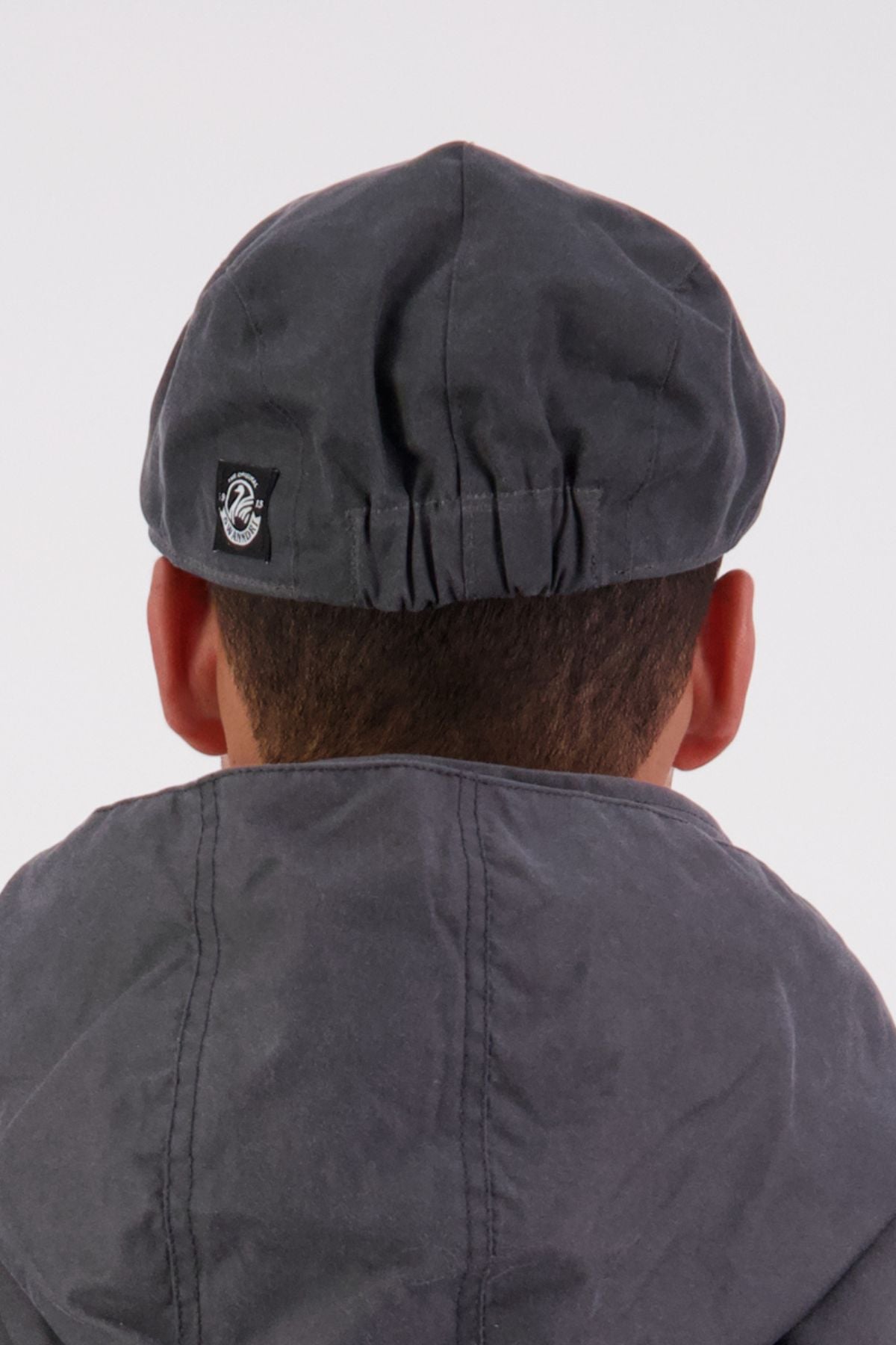 A person wearing a dark gray Swanndri Birmingham Oilskin Flat Cap and matching jacket, photographed from behind against a plain light background.