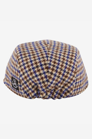 The Swanndri Bristol Flat Cap is a wool blend cap with a checkered pattern in brown, blue, and cream, finished with a small black logo tag on the side—an ideal outdoor accessory.