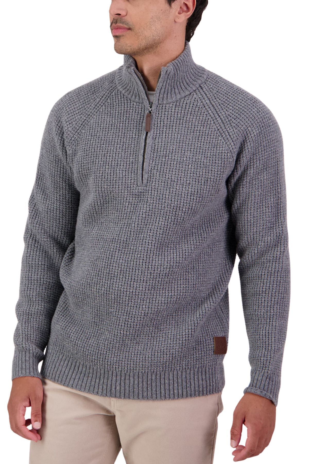A man stands looking to the side, wearing a Swanndri Chalky Island Waffle Jumper in gray with long sleeves and a half-zip collar, paired with tan pants.