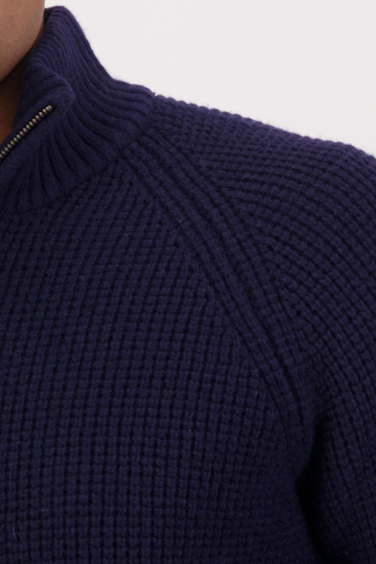 Close-up of a person wearing the Swanndri Chalky Island Waffle Jumper in dark blue, featuring a ribbed high collar and a half zip front. The cozy knit showcases a chunky texture. The person's face is not visible.
