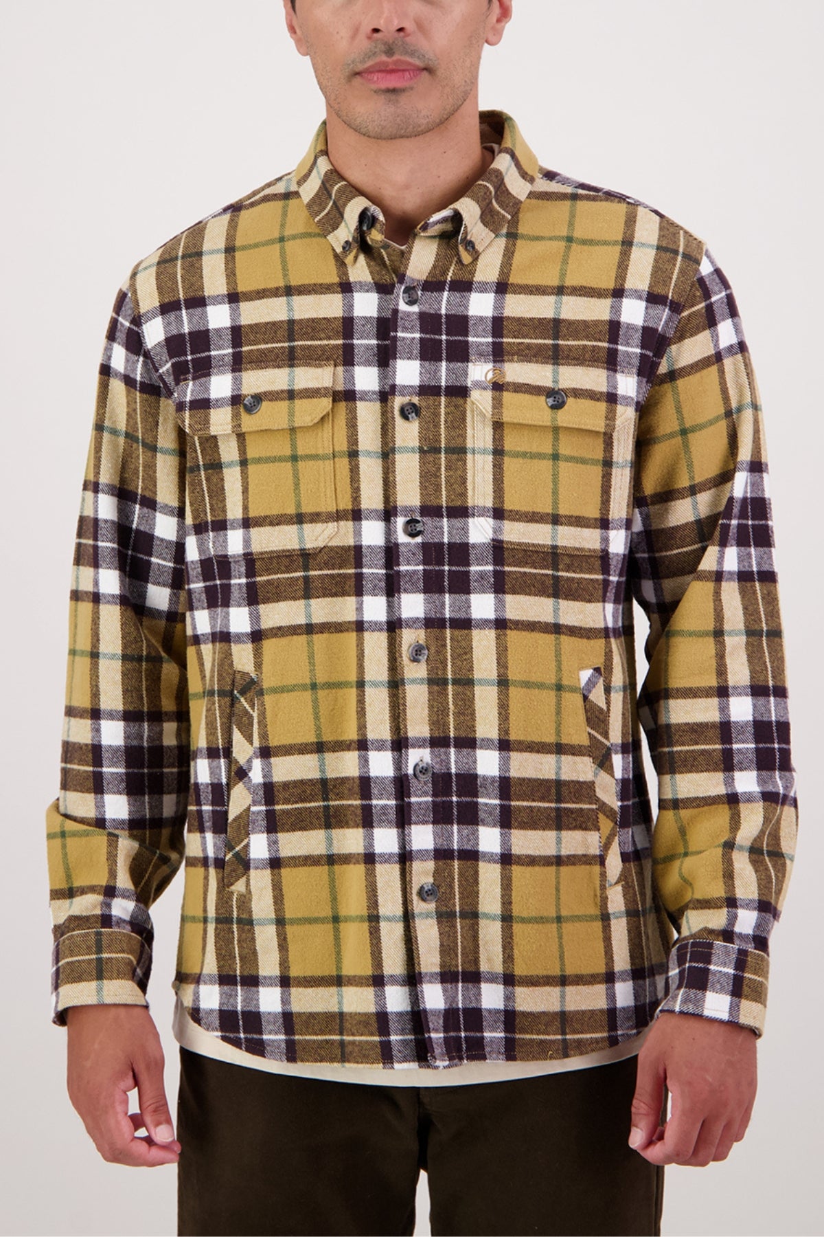A man in a Swanndri Crofton Shirt—100% cotton, yellow/brown/white plaid, with chest and side pockets—stands against a plain background, highlighting classic heritage workwear style.