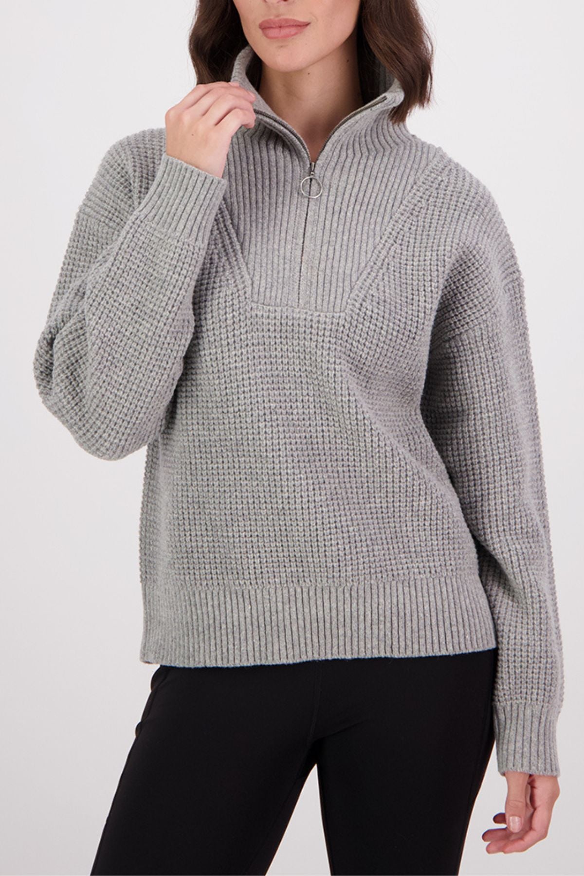 A woman wears a Swanndri Darlinghurst Zip Jumper—a light gray lambswool pullover with an oversized collar and long sleeves—paired with black pants. Only the lower part of her face is visible.