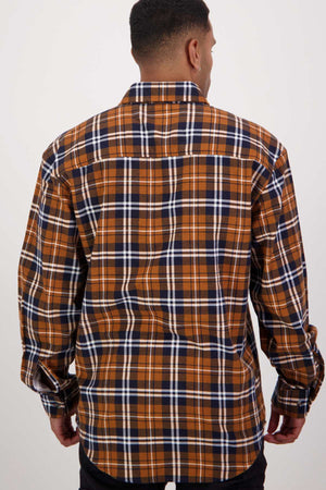 A person with short, dark hair is standing with their back to the camera, wearing one of the long-sleeve, button-down plaid shirts from the Swanndri Egmont Flannelette Twin Pack. The shirt is made of soft brushed cotton and features a pattern of brown, navy blue, and white checks against a plain white background.