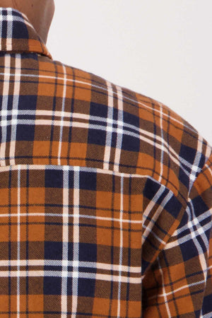 Close-up of a person wearing the Swanndri Egmont Flannelette Twin Pack shirt in a brown, blue, and white plaid pattern. The image focuses on the back and shoulder area of the flannelette shirt, highlighting the fabric pattern and texture.