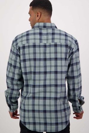 A man is seen from the back wearing a green and navy blue plaid long sleeve shirt from the Swanndri Egmont Flannelette Twin Pack. He has short hair and is standing against a plain white background.