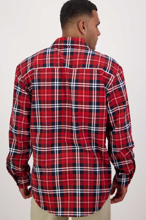 A person stands with their back to the camera, showcasing a Swanndri Egmont Flannelette Twin Pack long-sleeve shirt in a red, white, and black plaid pattern. The shirt features a classic design with intersecting lines, and the individual complements it with light-colored pants against a plain white background.
