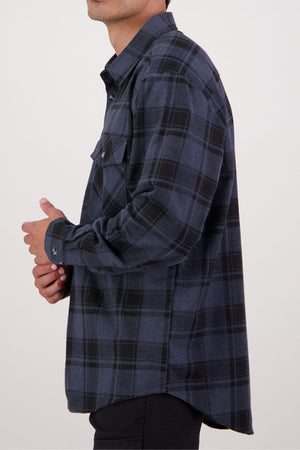 A person in the Swanndri Egmont Flannelette Twin Pack blue and black plaid long-sleeve shirt, made of heavy flannelette, is shown from the side against a plain white background.