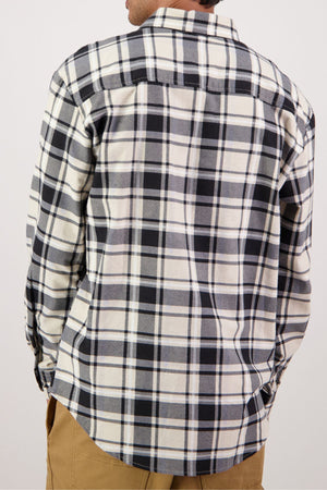 A person is shown from the back wearing an untucked Swanndri Egmont Flannelette shirt in a black, white, and gray plaid. The heavy brushed cotton long-sleeve shirt is paired with tan pants.