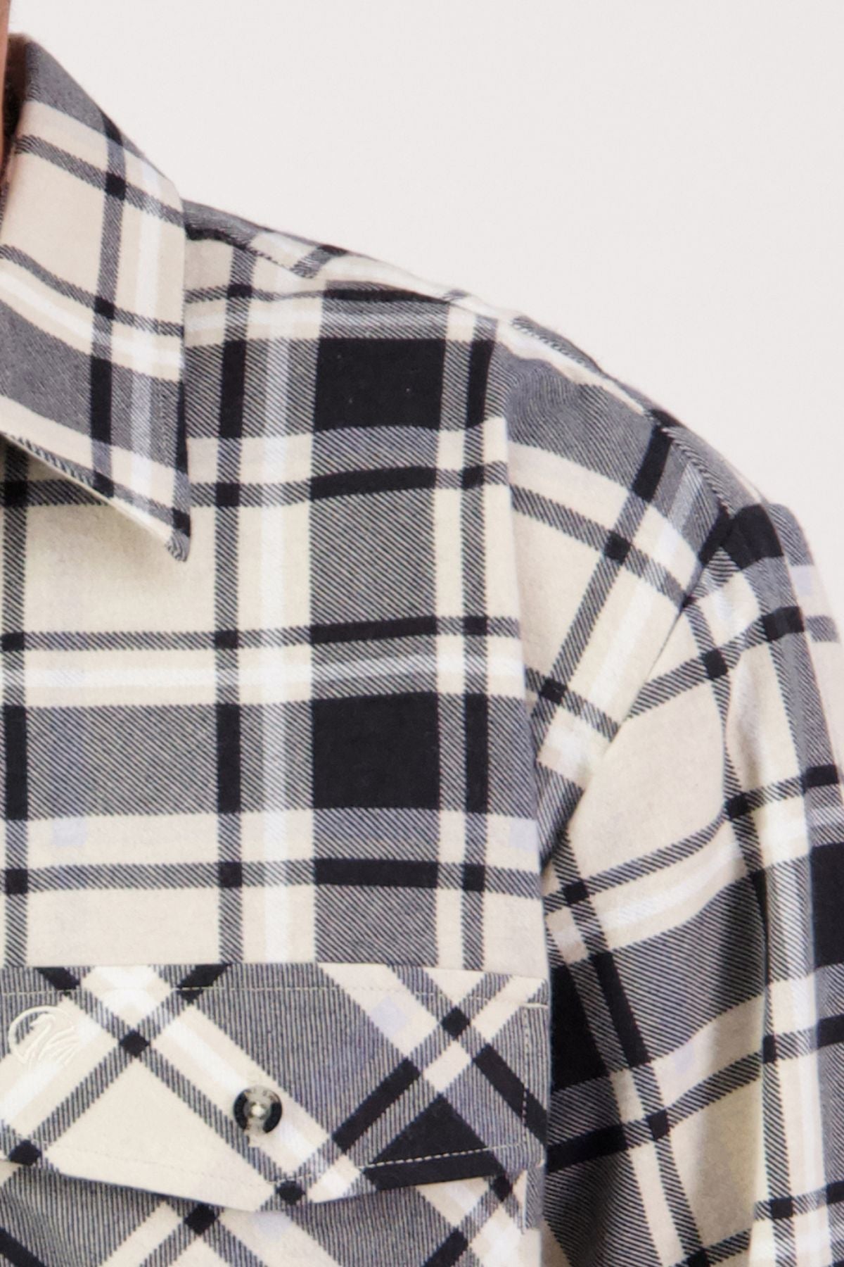 A close-up of the Swanndri Egmont Flannelette Twin Pack, featuring a black, white, and beige plaid shirt in soft brushed cotton. The image highlights the collar, shoulder, and buttoned chest pocket with intersecting lines and squares.