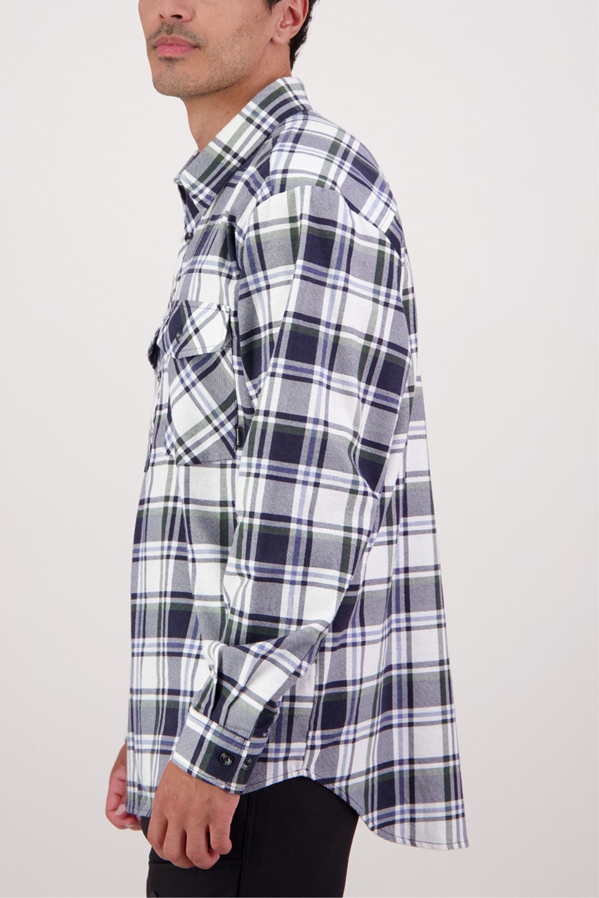 A person in a Swanndri Egmont Flannelette Twin Pack plaid long-sleeve shirt, featuring black, white, and green colors, stands sideways facing left against a plain light background.