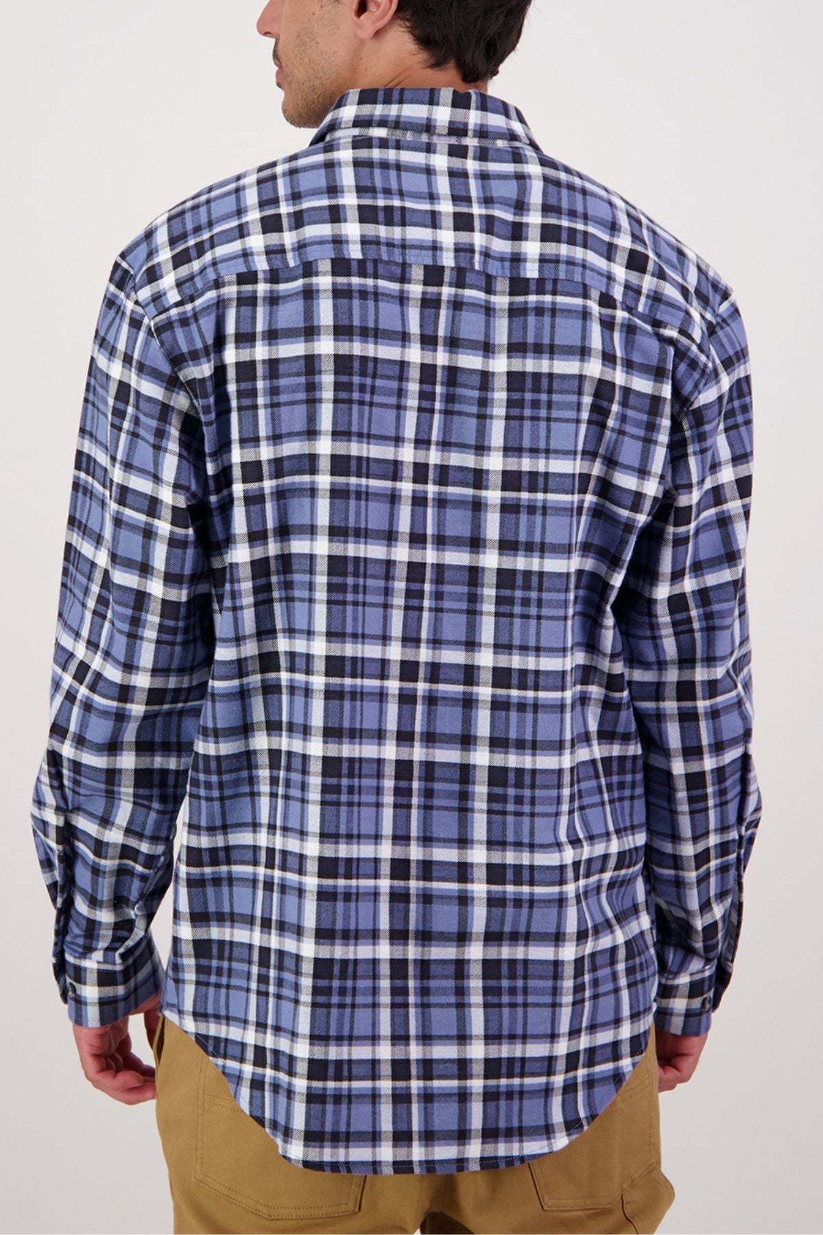 A person is seen from the back wearing the Swanndri Egmont Flannelette Twin Pack shirt in blue, black, and white plaid with tan pants against a plain background.