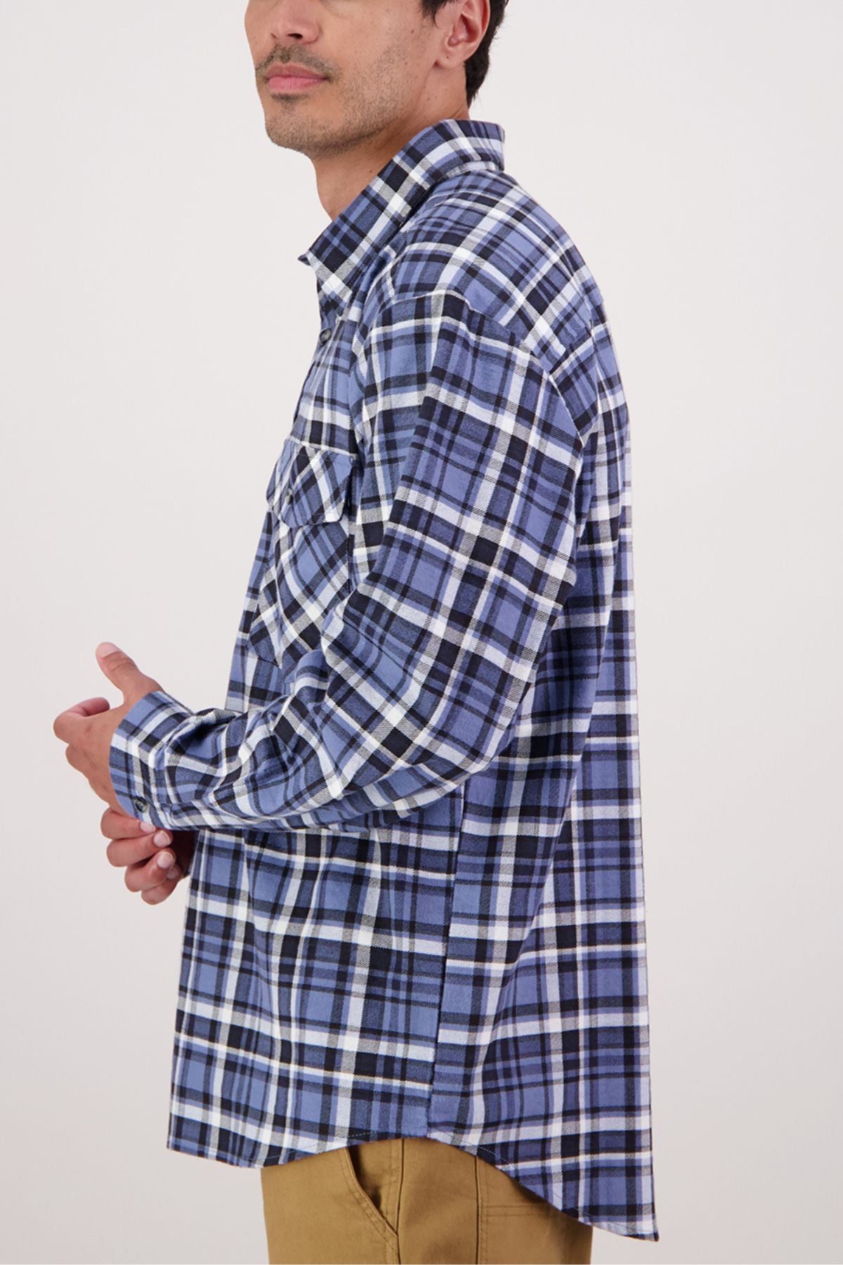 A man stands in profile against a plain light background, wearing the Swanndri Egmont Flannelette Twin Pack shirt in blue and white plaid with tan pants.