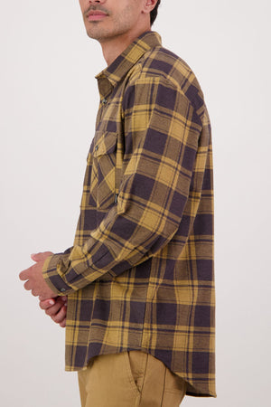 A man stands in profile against a light background, wearing a Swanndri Egmont Flannelette Twin Pack yellow and brown plaid long sleeve shirt with a chest pocket.