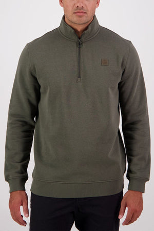 A man wears the Swanndri Fundamentals Quarter Zip in olive green, made from recycled polyester and featuring a small square logo on the left chest, standing against a plain white background.