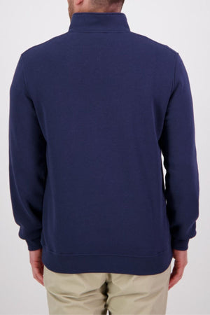 A man is seen from the back, wearing a navy Swanndri Fundamentals Quarter Zip and light beige pants, standing against a plain white background.