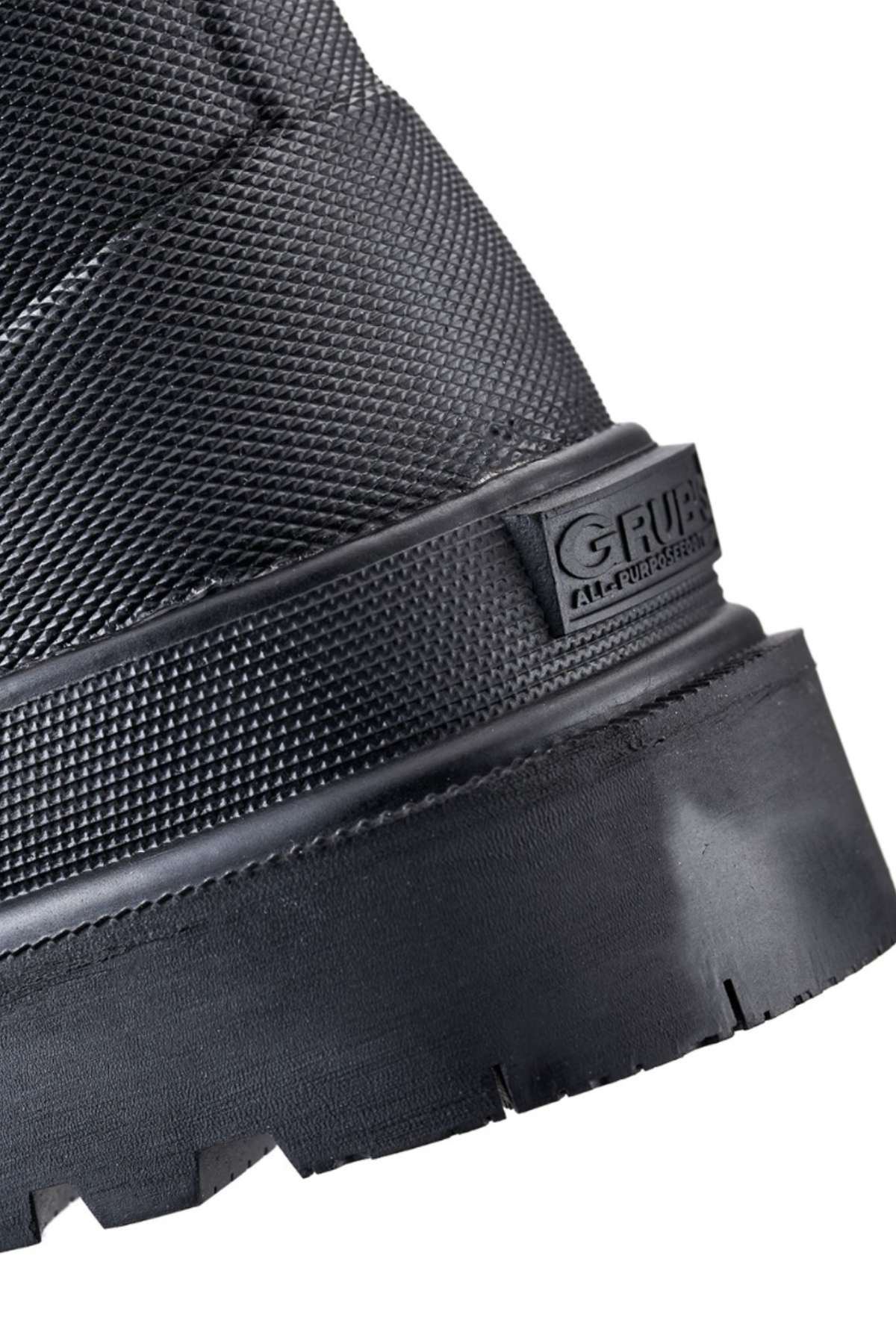 Close-up of a sturdy black Grubs Fenline High Work Boot with a textured surface, showcasing a thick sole and part of the heel. The brand "Grubs" is embossed on the side. The design features durable neoprene material and superior grip, suggesting the boot is intended for heavy-duty or outdoor use.