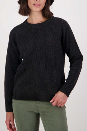 A woman wears the Swanndri Hayes Park Waffle Knit Crew with light green pants, standing against a plain light background, one hand on her hip and the other relaxed by her side.