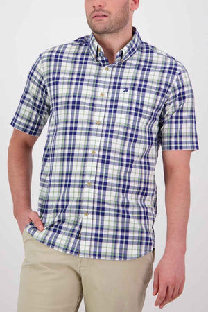 A man is wearing the Swanndri Herbert Short Sleeve Shirt, a tailored fit button-up crafted from blue and white plaid cotton fabric, featuring an embroidered logo on the chest. He casually places one hand in the pocket of his beige pants while standing against a plain white background.
