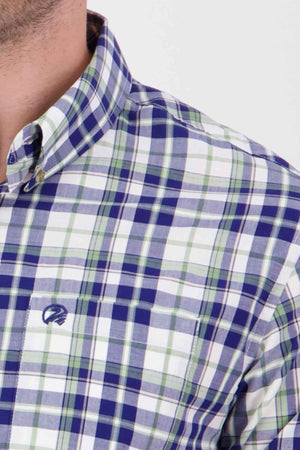 Close-up of a person wearing the Swanndri Herbert Short Sleeve Shirt, a tailored fit button-up cotton shirt in blue, green, and white plaid with an embroidered logo on the chest pocket. The shirt features a button-down collar, with only a partial view of the person's face visible.