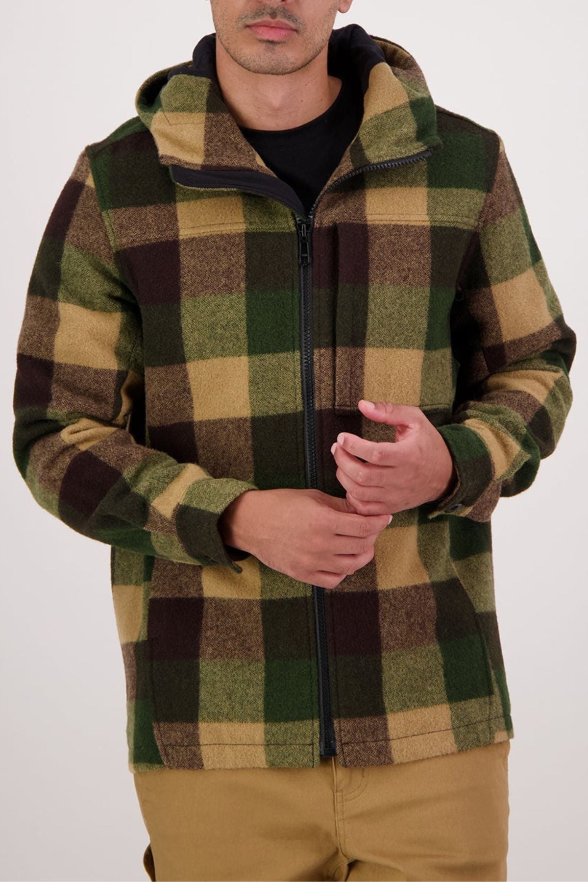 A person wearing a Swanndri Hudson Hoodie—a durable New Zealand wool jacket with a bold brown, green, and tan plaid—zipped over a black shirt. They have light skin and stand against a plain light background.