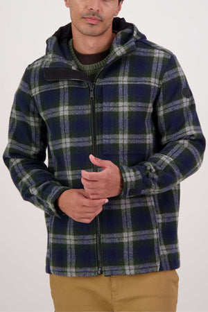 Wearing the Swanndri Hudson Hoodie—a green, blue, and white plaid jacket with a hood—over a green sweater and tan pants, this person highlights the hoodie’s classic style and durable warmth against a plain light background.