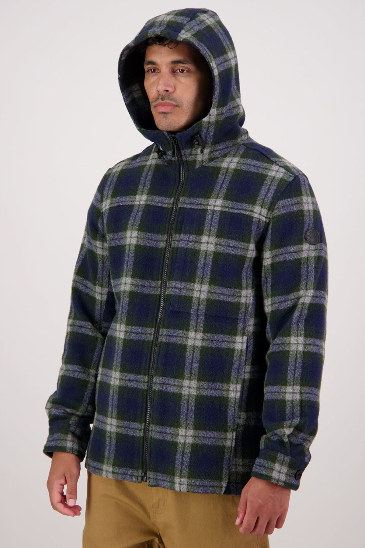 A person wearing a blue and green plaid Swanndri Hudson Hoodie with a front zipper and tan pants stands against a plain, light background.