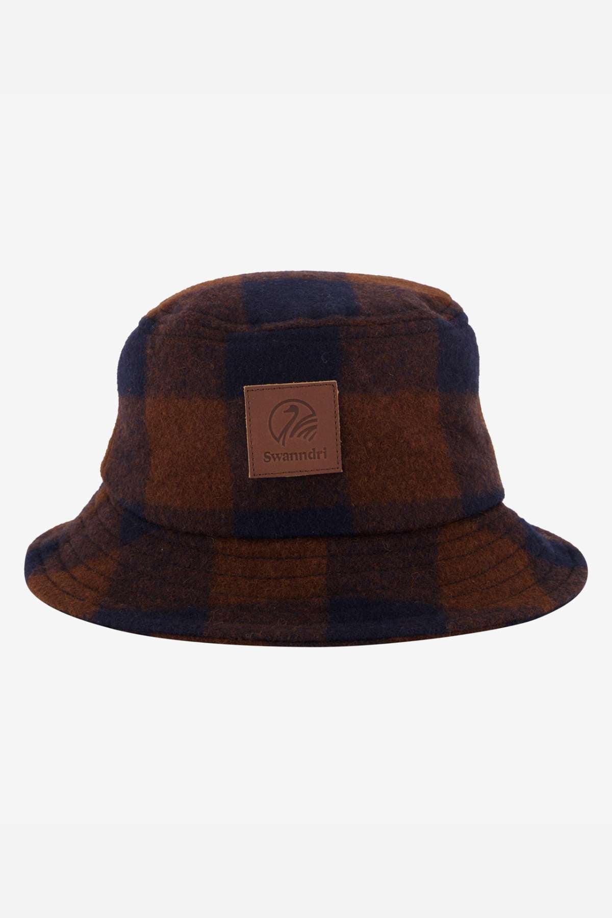 The Swanndri Kaimai Wool Bucket Hat showcases a brown and navy plaid design with a leather patch featuring the iconic "Swanndri" logo, perfect for outdoor adventures against a light gray backdrop.