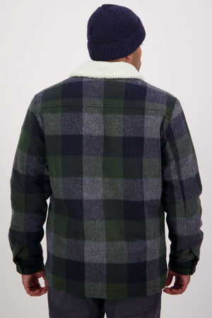 A person is seen from behind in a navy blue beanie and the Swanndri Kaituna Sherpa Lined Jacket, featuring a plaid pattern in green, navy, and gray hues. The jacket's fluffy white sherpa collar adds warmth. The background is plain and light-colored.
