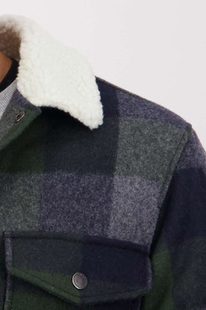 Close-up of the Swanndri Kaituna Sherpa Lined Jacket in green and gray plaid merino wool, showcasing its cozy white sherpa collar and lining, with a metal button and flap pocket on the chest.