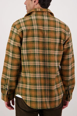 A person seen from behind wears the Swanndri Kiaraki V4 Wool Shacketโa brown, green, and beige plaid flannel shirt with heritage styling and dark buttonsโstanding against a plain light background.