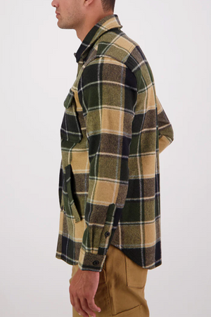 A man stands sideways wearing a Swanndri Kiaraki v3 Wool Shacket in green, black, and tan plaid with brown pants against a plain white background.