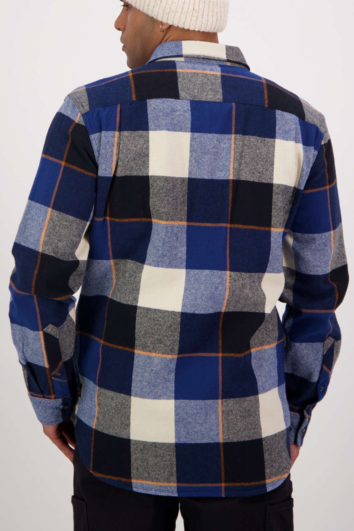 Someone is shown from the back against a plain light background, wearing the Swanndri Lowcliffe Shacket—a 100% cotton, classic fit shirt—in blue, black, gray, and white checks with a white knit beanie.