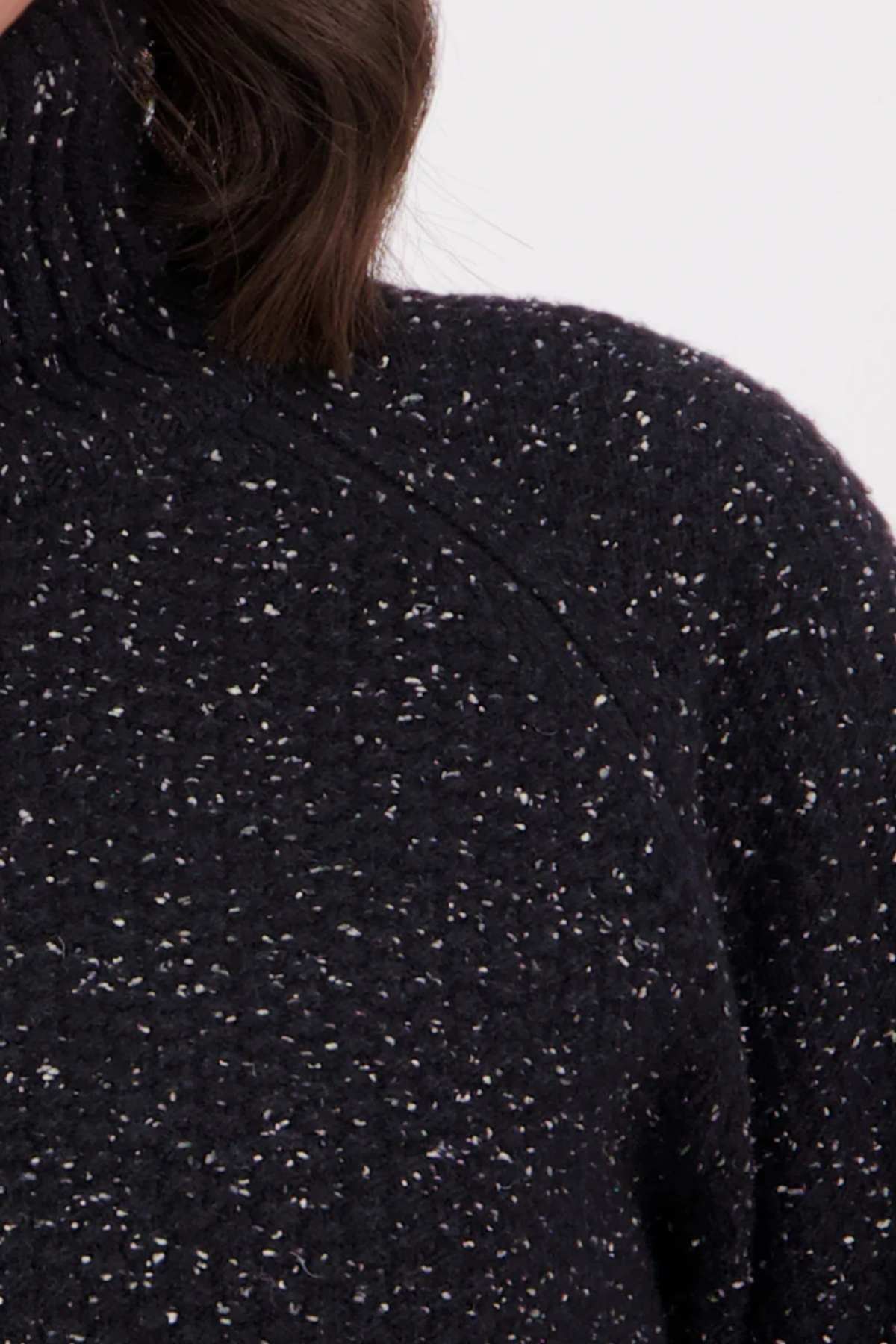 Close-up of a person wearing the Swanndri Lyttelton v2 Roll Neck Knit in black speckled lambswool. Only the shoulder, chest, neck, and some hair are visible against a plain background.