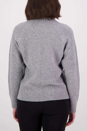 A person with shoulder-length brown hair is seen from behind, wearing the Swanndri Lyttelton v2 Roll Neck Knit in light gray with long sleeves and black pants, set against a plain white background.