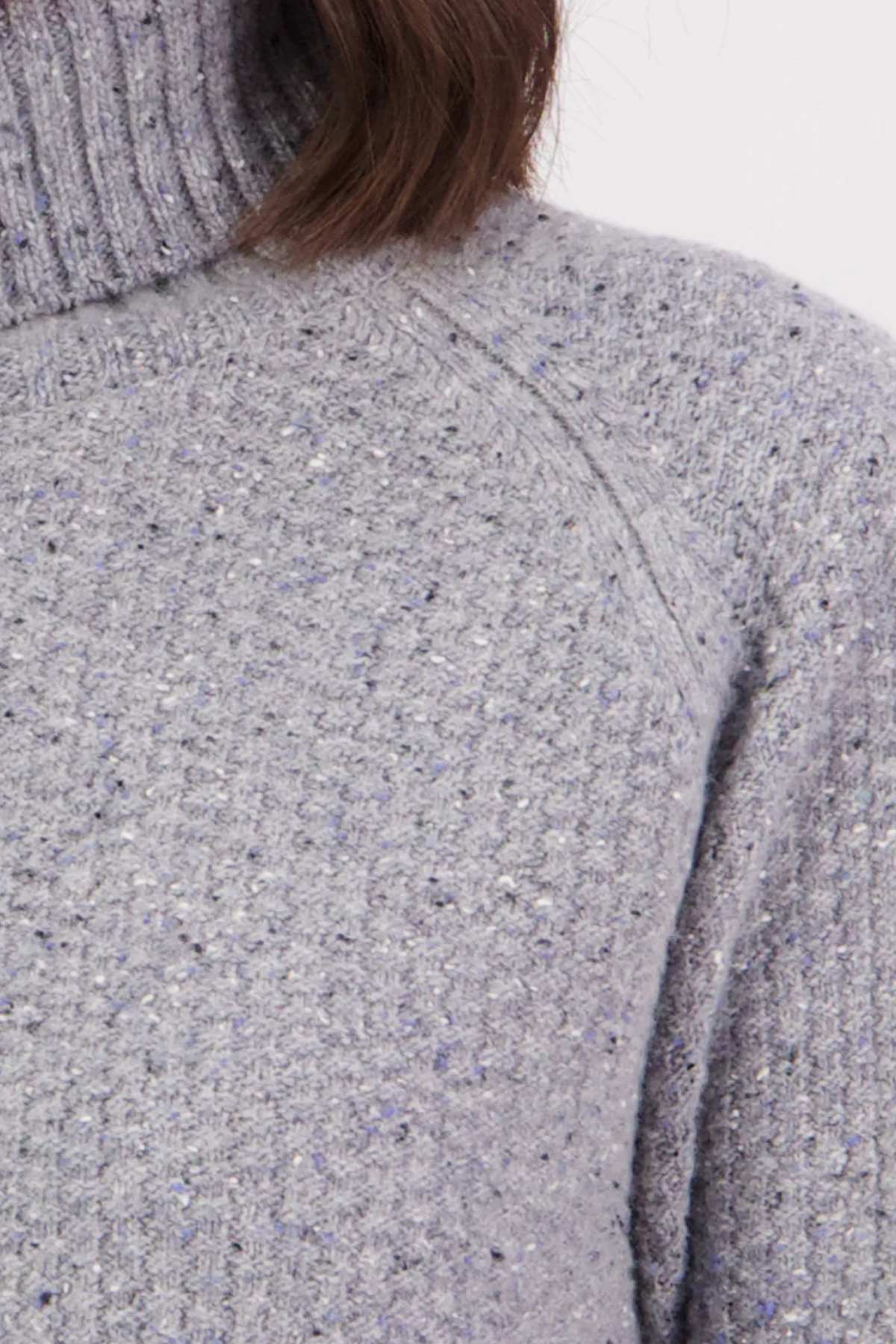 Close-up of the Swanndri Lyttelton v2 Roll Neck Knit in light grey lambswool with speckled texture and ribbed turtleneck, showing only the upper chest, shoulder, and part of the neck and hair.