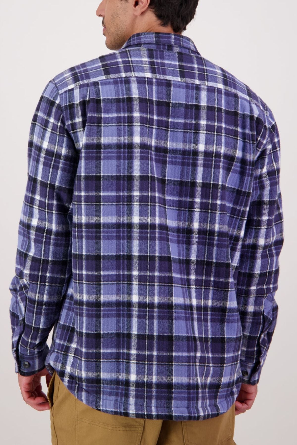A man is shown from the back against a plain light background, wearing a blue and purple plaid Swanndri Morven Sherpa Shirt with khaki pants.