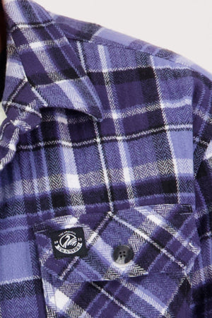 Close-up of the Swanndri Morven Sherpa Shirt in purple, black, and white plaid, featuring a buttoned breast pocket, a black and white logo tag above the flap, and warm ultra-soft sherpa fleece lining.
