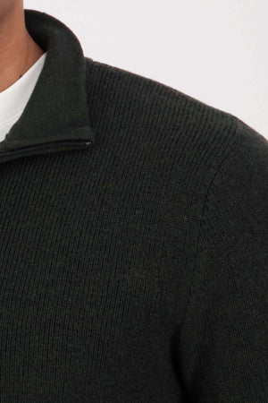 Close-up of a person wearing the Swanndri Otahu River Quarter Zip Merino Knit sweater with a short standing collar over a white shirt. Only the shoulder, upper chest, and part of the neck are visible.