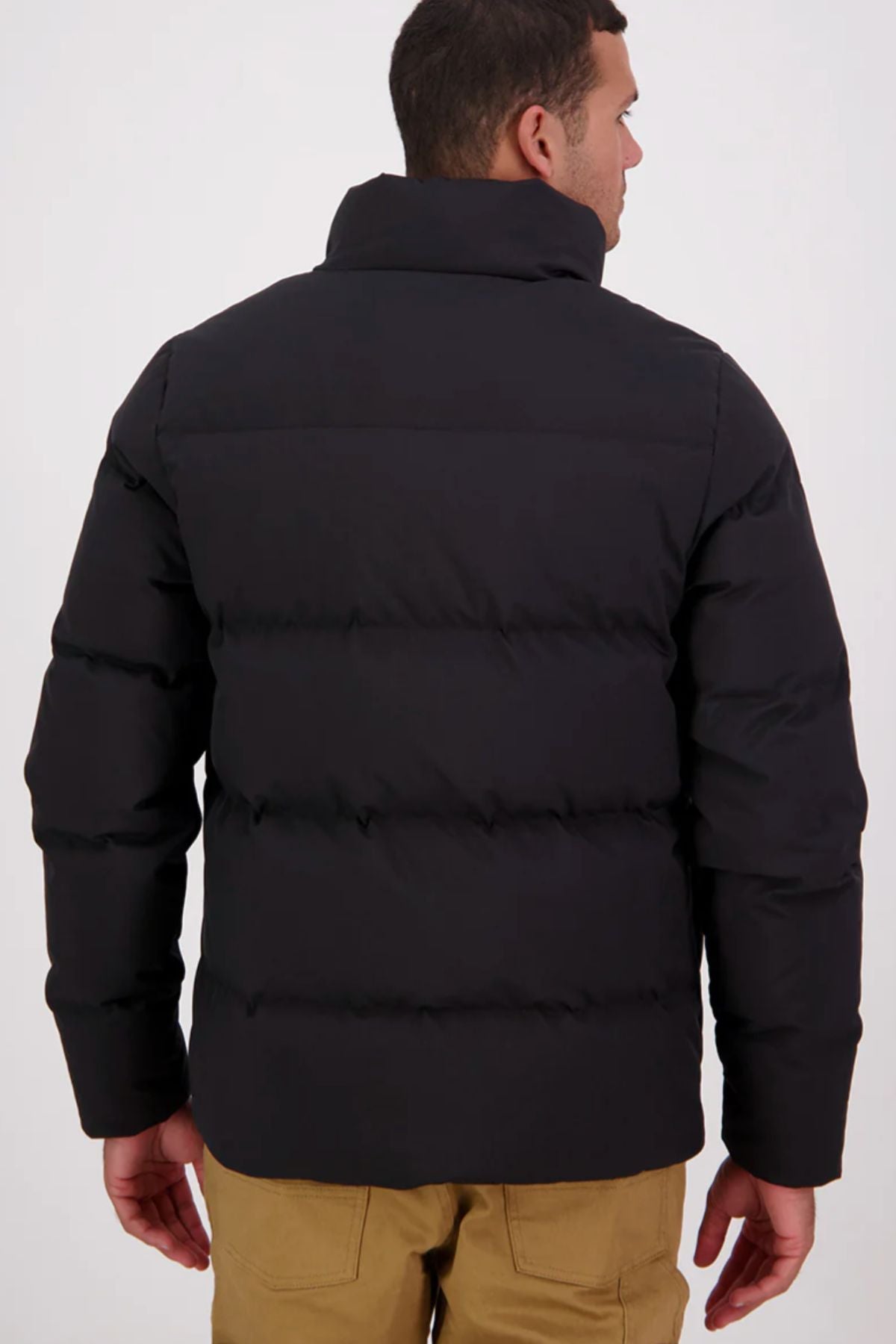 A man stands with his back to the camera wearing the Swanndri Plume Mens Down Jacket and tan pants against a plain light background—ideal for outdoor activities.