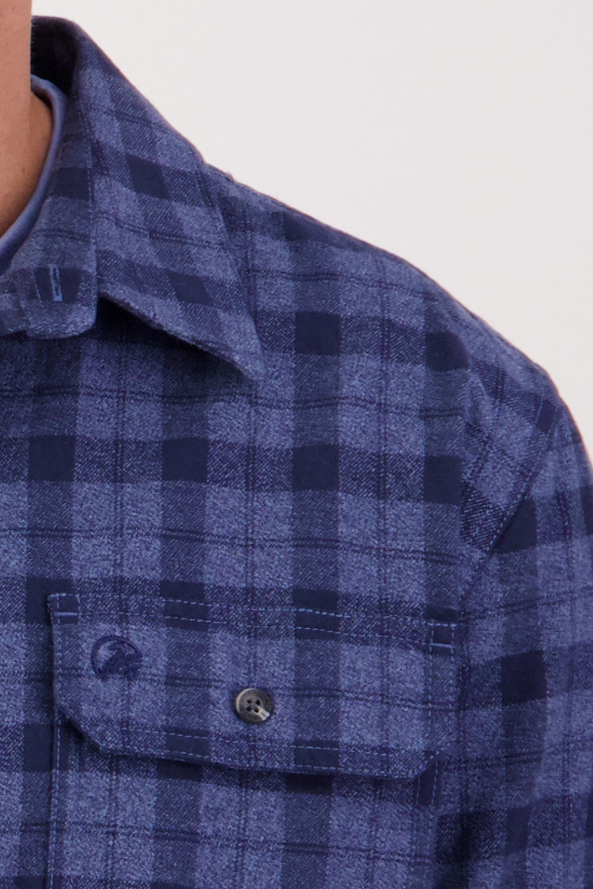 Close-up of a person wearing the Swanndri Port Road Shirt in blue and navy, made from heavy weight twill with a buttoned chest pocket and collar. Only part of the neck and shoulder are visible against a plain background.
