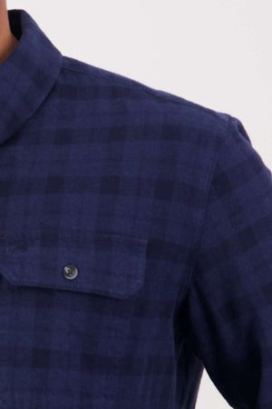 Close-up of the Swanndri Port Road Shirt in navy blue plaid, featuring a buttoned chest pocket and heavy weight twill on the upper left side, shoulder, and collar against a plain light background.