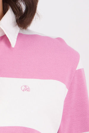 A close-up of a person with chin-length brown hair wearing a pink and white striped Swanndri Ridgeway Womens Rugby shirt, made from 100% cotton, featuring a small embroidered logo on the chest.