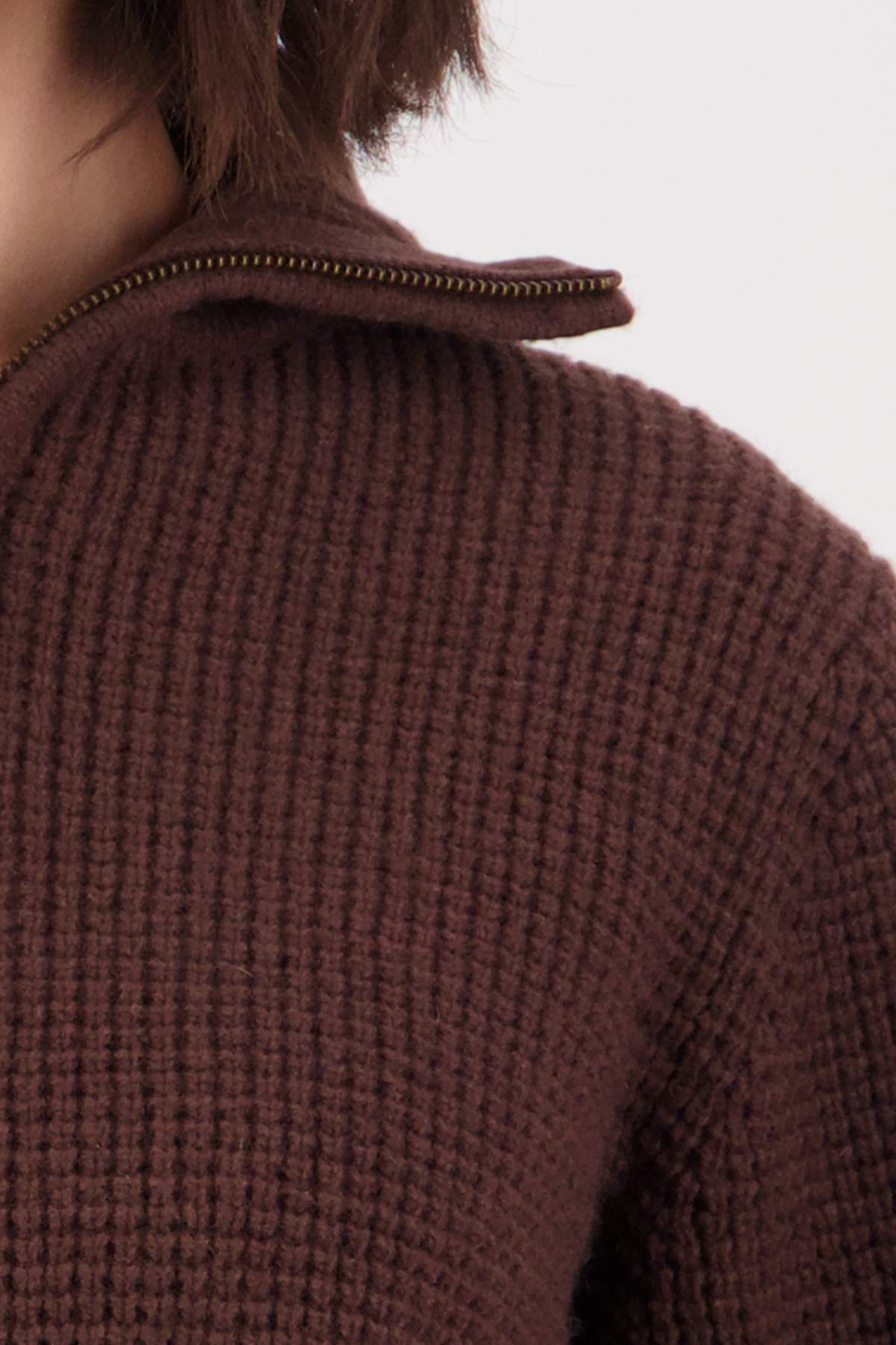 Close-up of a person wearing the Swanndri Riverside v2 Zip Neck Rib Jumper in dark brown lambswool; only the shoulder, chest, and neck are visible, along with short brown hair.
