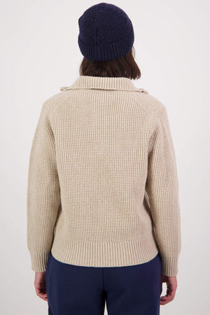 Rear view of a person in a cozy Swanndri Riverside v2 Zip Neck Rib Jumper and dark beanie against a plain backdrop. They have shoulder-length hair and are wearing dark pants.