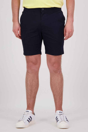 A person wearing navy blue Swanndri Sandy Point Shorts, crafted from a cotton stretch fabric, and white sneakers with black stripes stands in front of a plain background. While their upper body is not shown, the shorts are highlighted by their multiple pockets for added versatility.