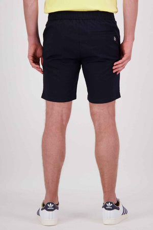 Rear view of a person wearing a yellow shirt, Swanndri Sandy Point shorts in black with multiple pockets, and blue Adidas sneakers with white stripes, standing against a plain light background.